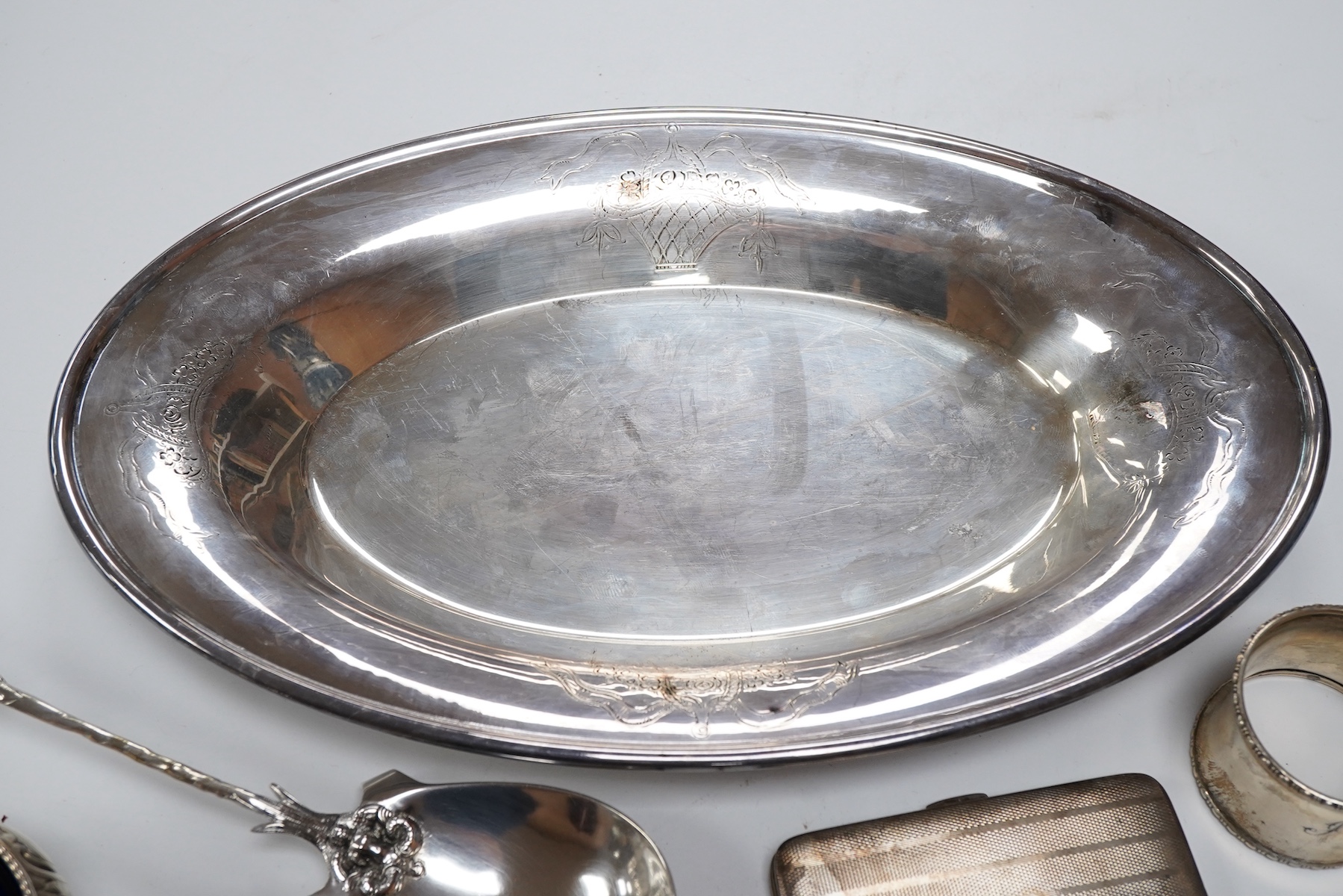 A Victorian silver bun salt, London, 1860, a later silver cigarette case, a silver napkin ring and pair of silver sugar tongs, together with a continental white metal serving spoon and a silver plated oval tray.